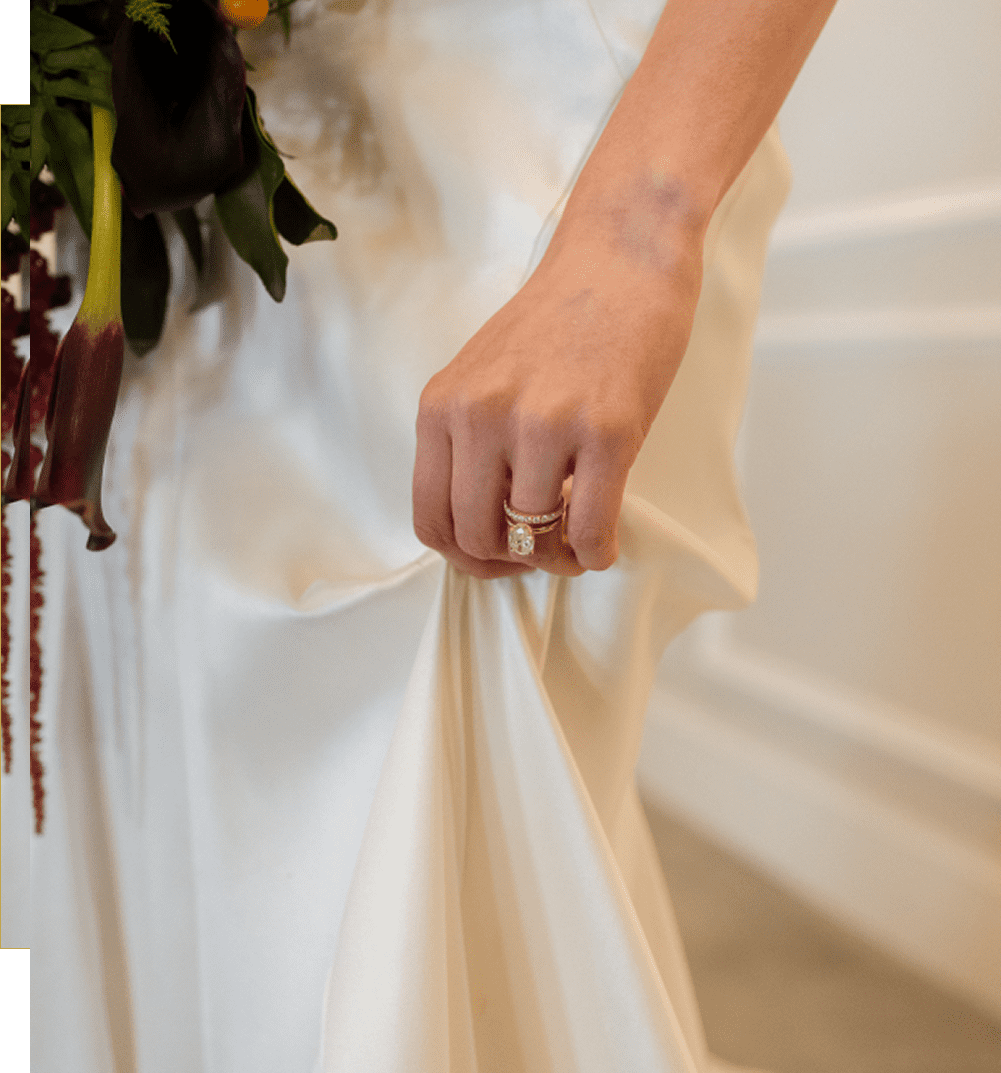Close-up of a bride holding her wedding dress, showing a delicate ring.