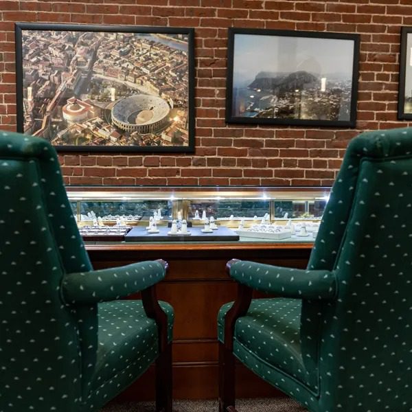 Two green armchairs facing a chessboard on a wooden table with framed pictures on a brick wall.